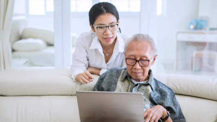 young woman helping elderly man with laptop